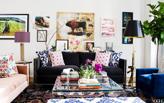  NYC apartment with madeline weinrib throw pillows on a charcoal gray velvet sofa with nailhead trim, glass coffee table, brass floor lamp, large patterned rug with walls covered in art