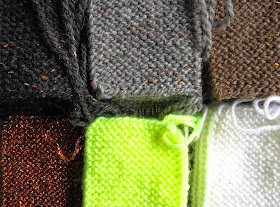 Rows of garter-stitch knitted rectangles in earth colours with shots of gold, and in bright white and neon yellow.