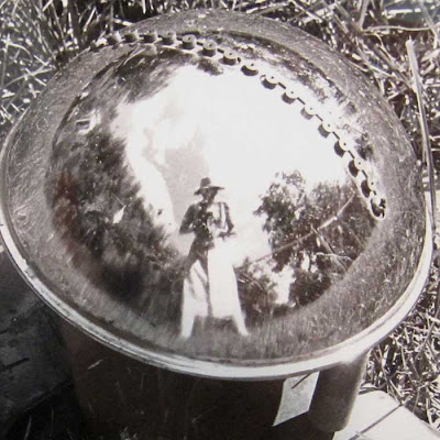 Photo of a shiny half-spherical sprinkler in grass, woman with camera reflected in it