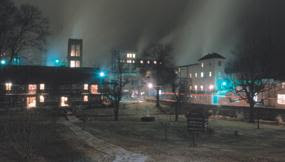 a spooky view of the distillery buildings a night with lights showing through fog