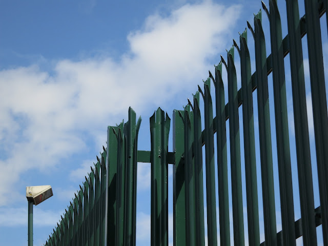 Spiked Metal Security Fence, Lampost and Blue Sky with Clouds