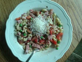 A bowl of elbow pasta, ham, tomato, green peas, red bell peppers, & red onion