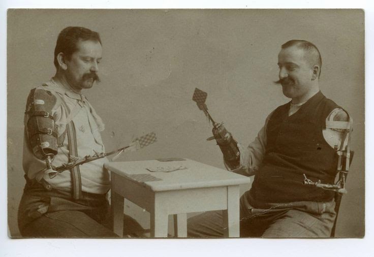 Old brown-tone photo of two men, both with prosthetic arms, playing cards.