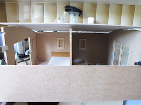 Front view of a dolls; house miniature shed kit, held together with clamps and tape, with a piece across the front.