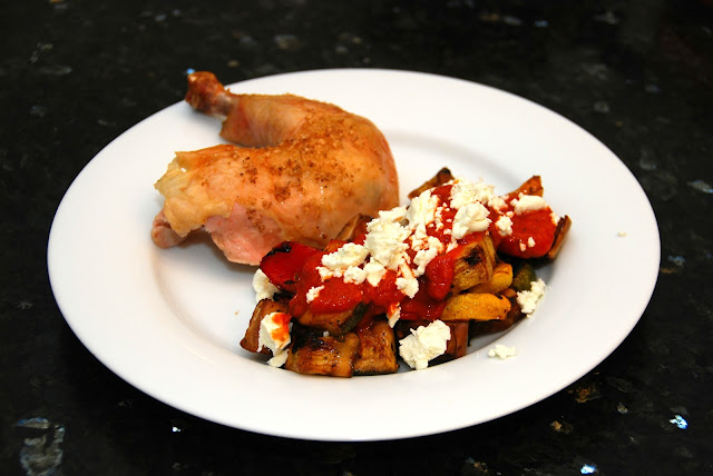 roasted chicken leg with roasted veggies topped with goat cheese on white plate