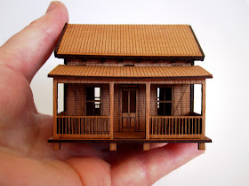 Wooden laser-cut miniature wooden cottage, held by a hand.