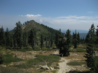 Hiker on rocky trail through a meadow, with Mt. Shasta in the distance, on the way to Heart Lake, Mt. Shasta, California