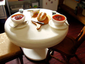 Dolls house miniature table set with two bowls of soup and glasses of wine, and a loaf of crusty bread