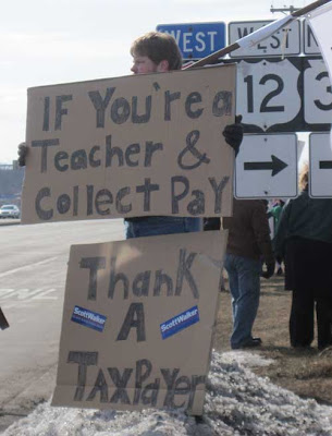 Counter demonstrator with two large signs reading If you're a teacher & collect pay thank a taxpayer, with two Scott Walker bumper stickers attached