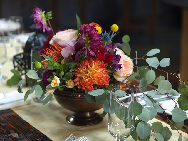 Moroccan inspired wedding centerpiece with orange, purple and fuchsia blooms. Featuring dahlias, phlox, garden rose, prothea, eucalyptus, thistle and spray roses.