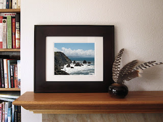 A photo of the Pacific ocean's waves crashing into the rocky coastline with a beautiful sunny blue California sky and dramatic distant rain clouds in the background.