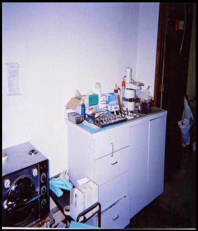 Freestanding cabinet with cluttered countertop. Amid the clutter is a food processor. Nearby is an autoclave.