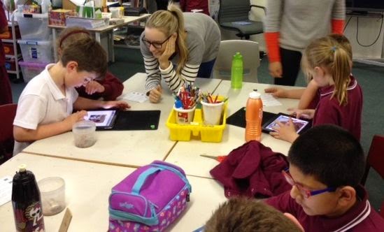 children working on iPads in pairs, communicating with each other about their work