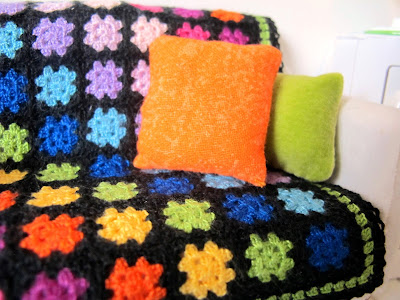 Modern dolls' house miniature rainbow crocheted afghan rug and bright cushions on a white sofa.