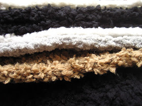 Stack of modern dolls' house miniature fluffy rugs in white, grey, black and fawn.