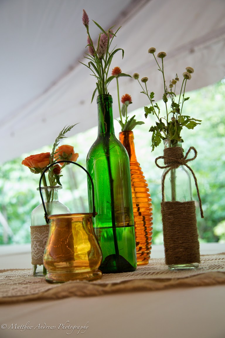 Bottles and bud vases with fever few, spray roses, celosia, and gomphrena placed on a burlap and lace table run mokarafloral.com