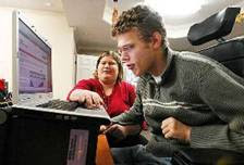 Boy reading at a computer with teacher in the background.