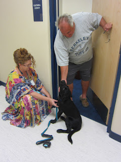 I'm kneeling by Coach, who is seated and looking up at Coach Dom. Dom has just opened his office door and is seeing his namesake for the first time. I'm kneeling by Coach, who is seated and looking up at Coach Dom. Dom has just opened his office door and is seeing his namesake for the first time.
