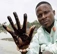Eric Dooh holds up a hand covered in oil from a creek near his former home, the now abandoned village of Goi.