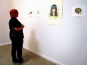 Woman standing in front of several coloured sketches in a gallery.