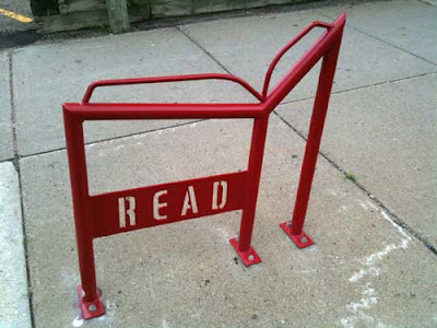Red metal bike rack shaped like an open book with the word READ in open stencil letters