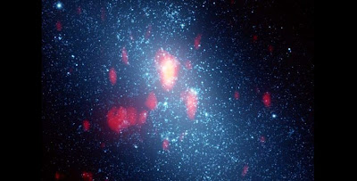 The blue background is a Hubble Space Telescope image of galaxy NGC 5253; the white spots are young star clusters. Superimposed is the gas (fuzzy red to yellow) as seen by the Submillimeter Array. The brightest part of the image is Cloud D. Credit: Jean Turner