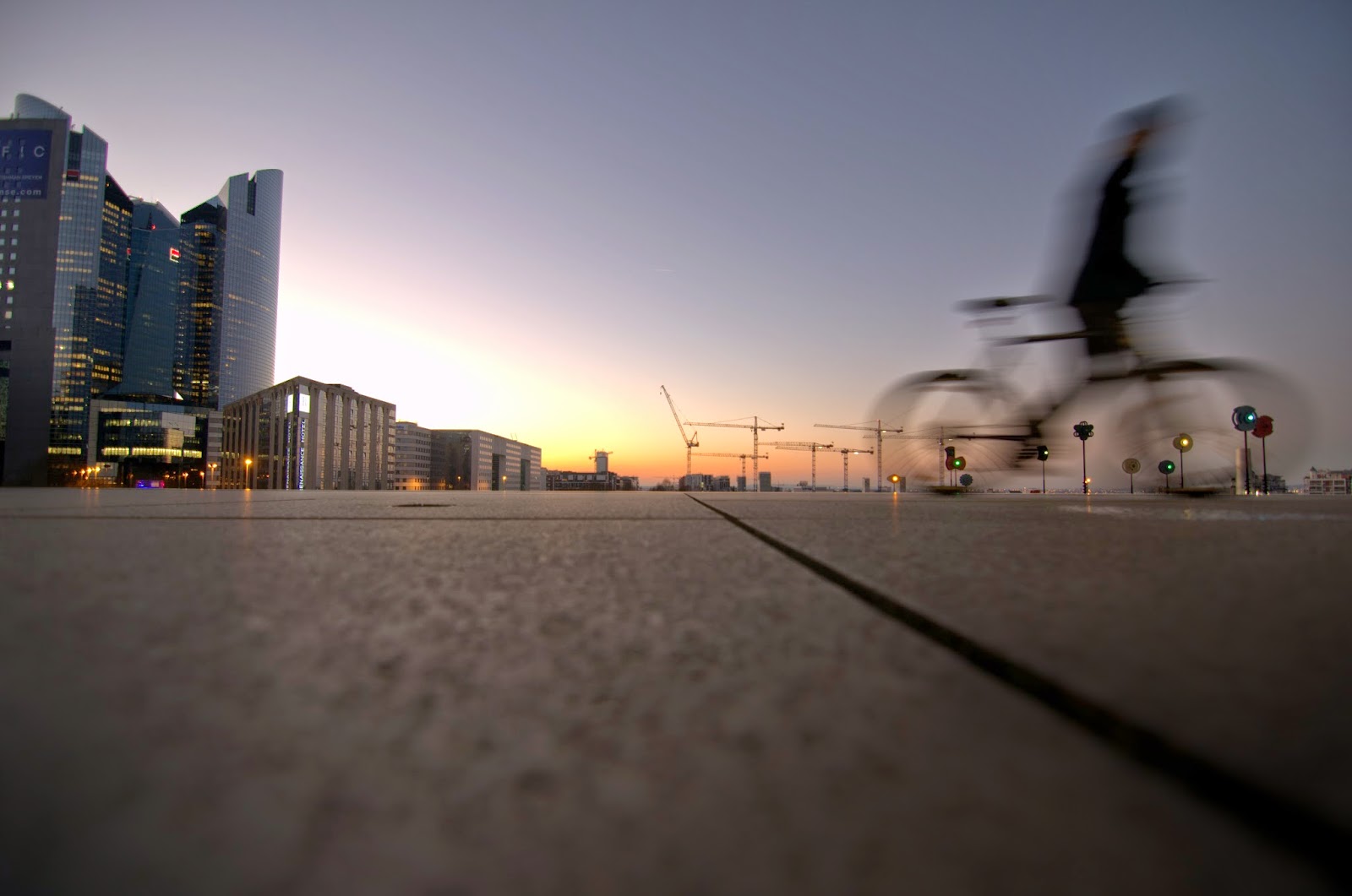 Un ciclista sfrecciante dietro La Grande Arche - © www.parisdailyphoto.com