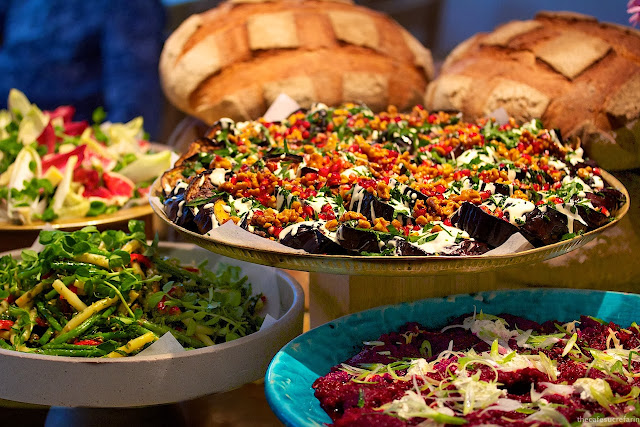 Everyday London - thecafesucrefarine.com Photo of large platters of lunch vegetable entrees with loaves of bread in the background at Nopi in London, England.