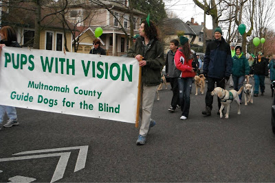 raisers carry a banner titled Pups with Vision, following behind them march more raisers and their puppies