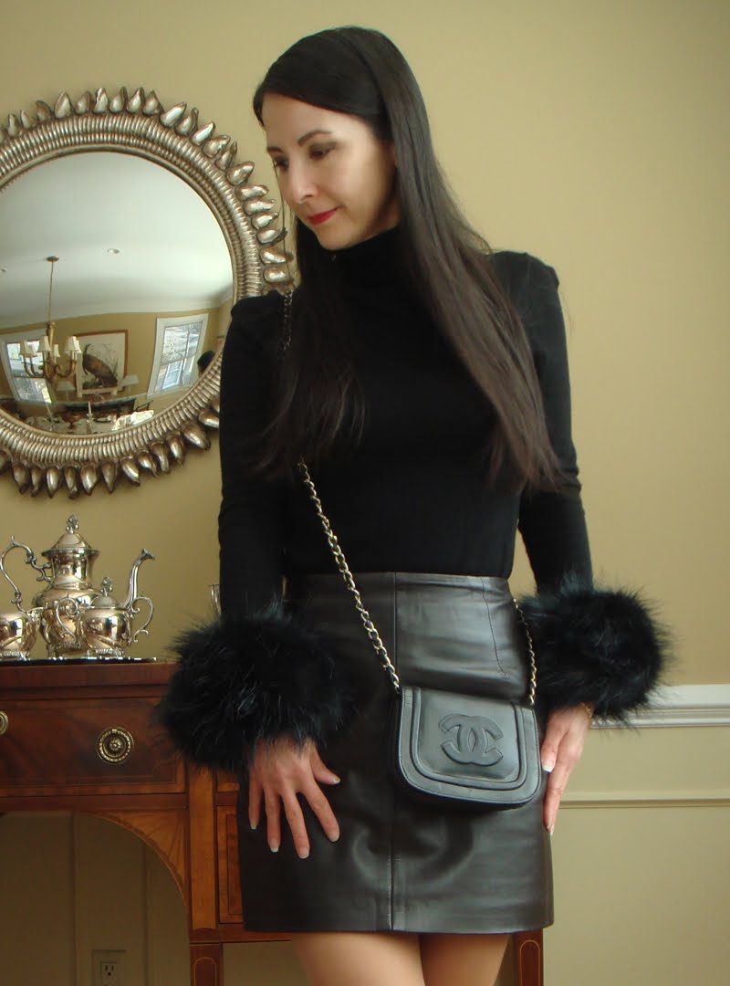How to Wear Faux Fur Cuffs Black faux fur cuffs on the sleeves of a black turtleneck with a leather skirt and black crossbody.