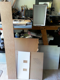 Four offcuts of MDF, in various sizes, leaning against a workbench in a house.