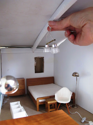 Woman holding a miniature light up to the ceiling of a dry-fitted modern miniature doll's house shed.