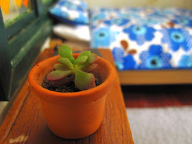 Miniature succulent in a pot on a table in a dolls house bedroom.