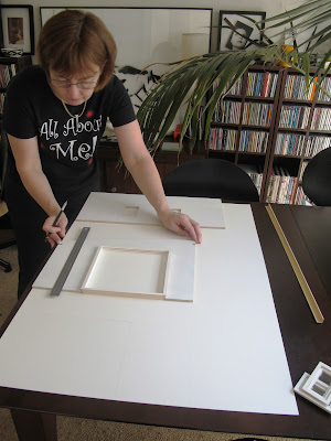 Woman tracing dolls' house kit walls onto of a large piece of mat board.