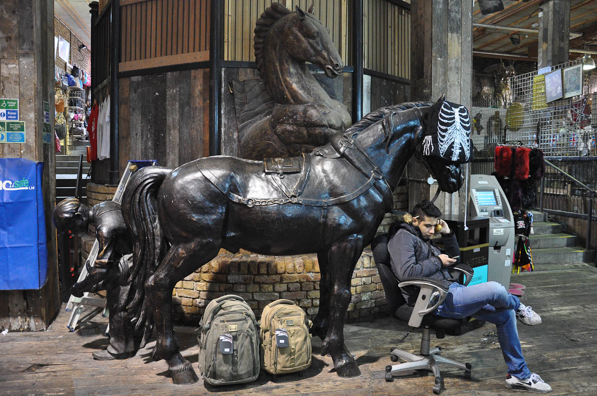 A market trader checking his phone by statue of horses, The Stables Market, Camden Town, London, England