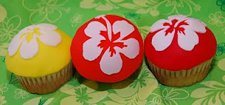 red, orange, and yellow fondant covered cupcakes with white hibiscus fondant decoration