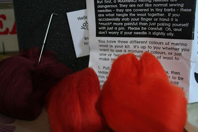 Needle Felting Kit a photo of orange and maroon roving wool and a foam block with a needle for needle felting.