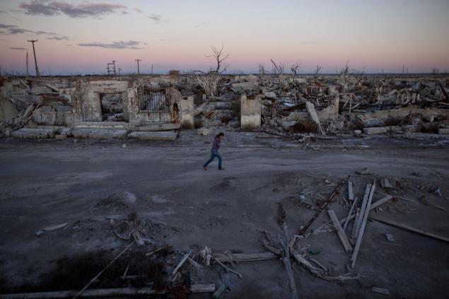 Former resident and tourist guide Norma Berg walks by a street in Epecuen. People come to see the rusted hulks of automobiles and furniture, crumbled homes and broken appliances.