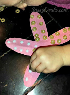kid gluing cheerios onto a pink paper starfish