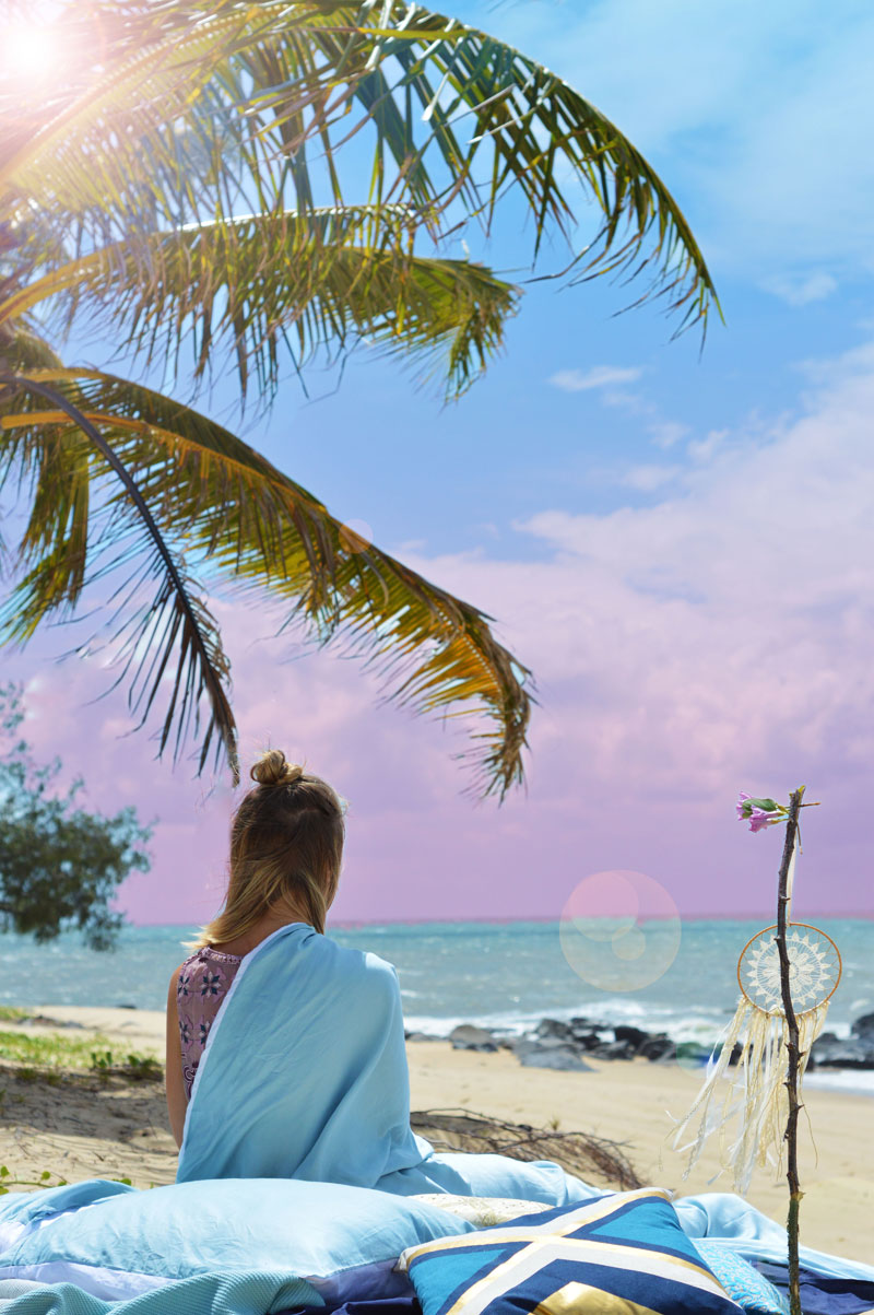 girl in pastel blue bedding under palm tree on far north queensland beach watching sunrise over sea girl in pastel blue bedding under palm tree on far north queensland beach watching sunrise over sea