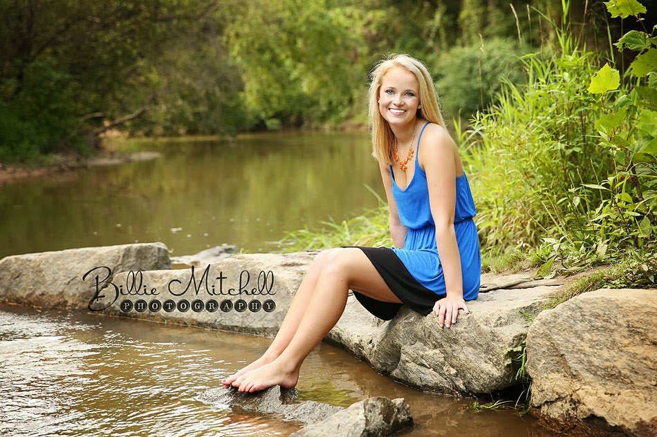 blonde senior girl in blue sundress sitting on rocks in creek
