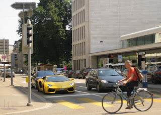 Cyclist pedals past a yellow Lamborghini Aventador stopped at a traffic light in Zürich, Switzerland.