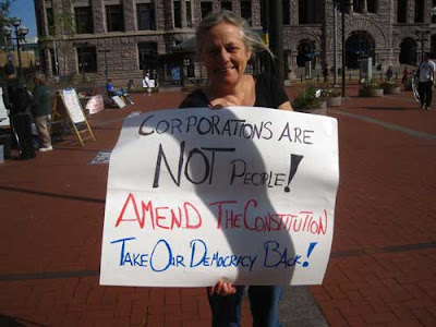 Woman holding sign that says the the idea corporations are people idea undermines democracy