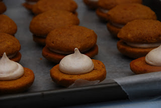 close up of unfinished sandwiches cookies with piped filling in front of finished whoopee pies on baking tray