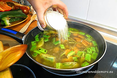 Echando el arroz en la sartén con el caldo y las verduras