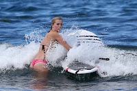 Ireland Baldwin in the ocean holding on to a paddle-board