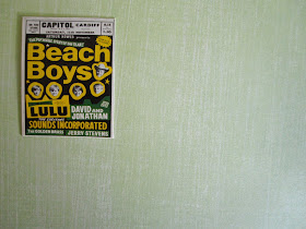 Bright 1960s Beach Boys poster  on a green wall.
