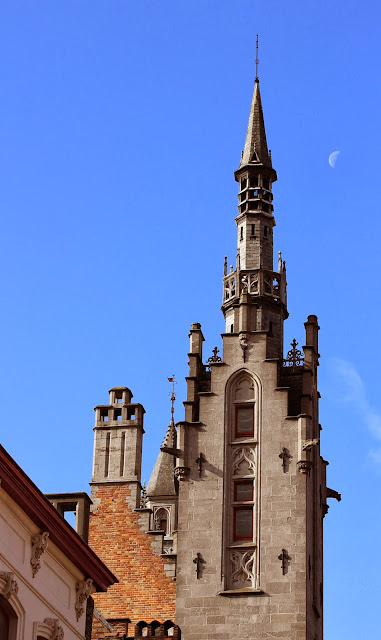 Sun and Moon Tower on the edge of the Burg in Bruge against a blue sky with the moon in the background