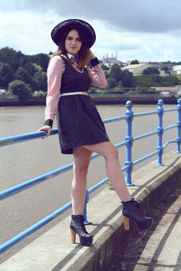 girl by the water front wearing leather pinafore, cowgirl pink shirt with white collar and white belt, large rim felt hat, frilly socks and jeffrey campbell boots uk fashion style, fashion blog, fashion styling, dahlia cowgirl shirt, lace shirt, leather pinafore, leather dress, large rim woollen hat, vintage woollen hat, vintage white waist belt, vintage photo, style by the water, rachael, poses with roses
