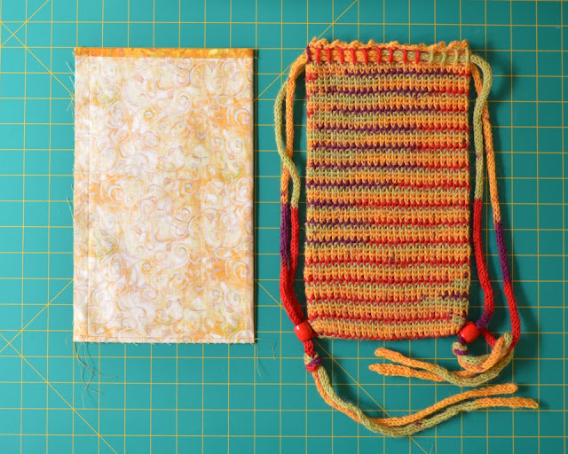 The lining is laid out next to the crocheted bag on the grid.